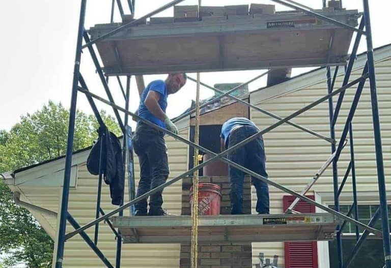 Masons rebuilding a tall chimney from scaffolding